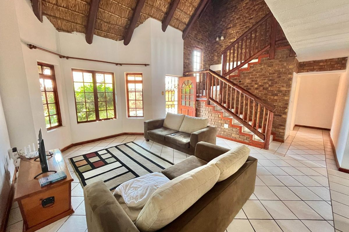 Spacious living room featuring a high thatched ceiling with exposed beams, a striking exposed brick wall, and a wooden staircase.