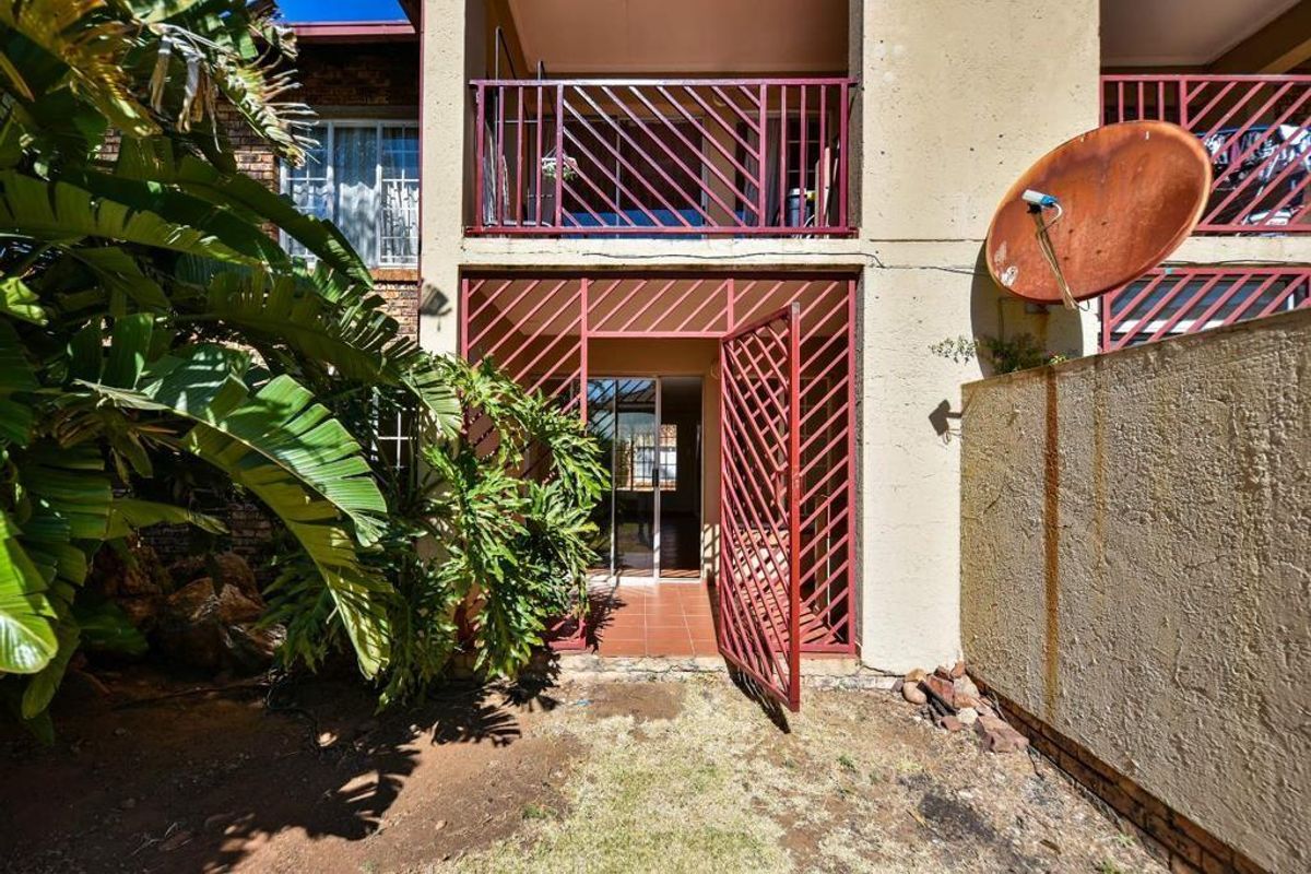 Rear view of the townhouse featuring a ground floor patio with security gate, an upper balcony, and a small garden area.