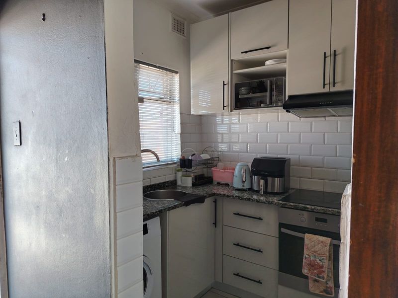 Compact kitchen featuring white cabinetry, granite countertops, subway tile backsplash, and integrated appliances including an oven and cooktop.