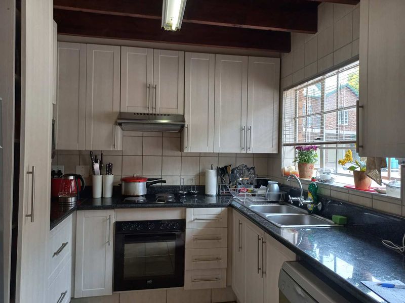 Functional kitchen featuring light-toned cabinetry, granite countertops, built-in oven, hob, extractor fan, and exposed timber ceiling beams.