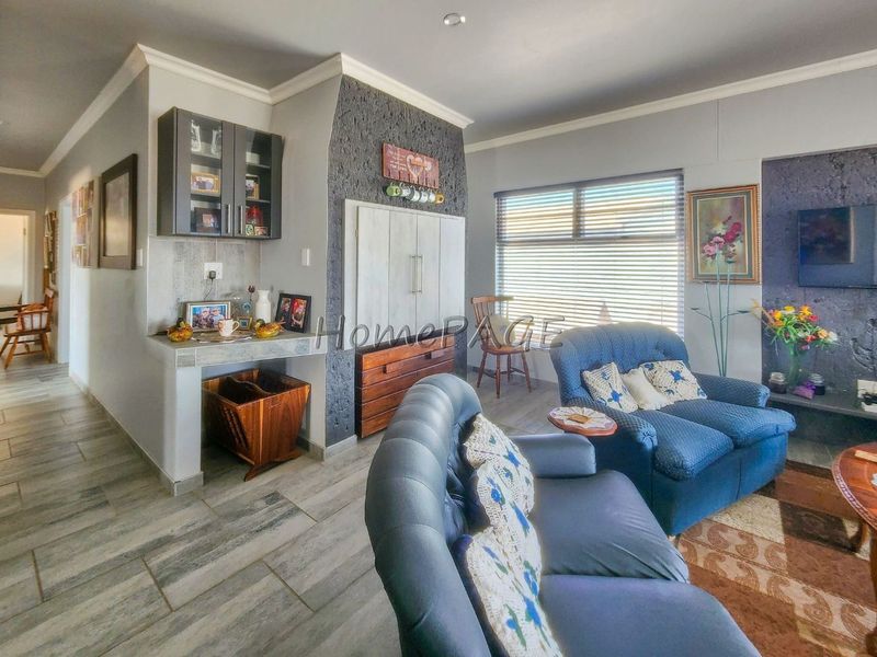 A comfortable living room featuring a stone-cladding accent wall, built-in cabinetry, and tiled flooring with natural light from large windows.
