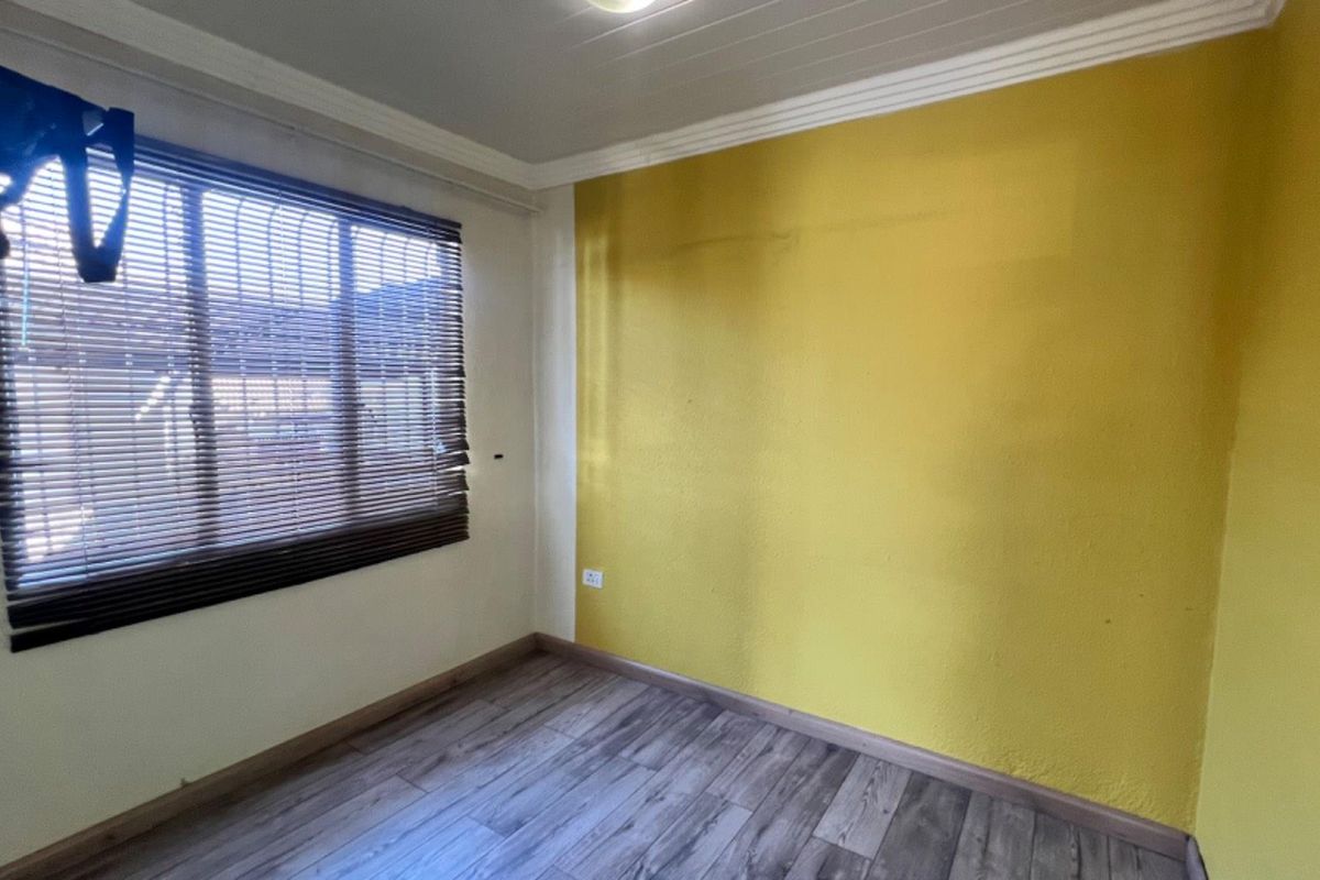 An empty bedroom featuring wood-look laminate flooring, a tongue and groove ceiling with cornicing, and a window fitted with venetian blinds.