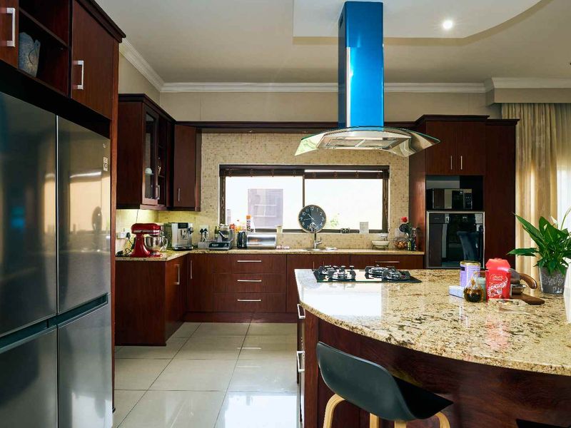 Spacious kitchen featuring dark wood cabinetry, granite countertops, a central island with a gas hob, and a modern stainless steel extractor fan.