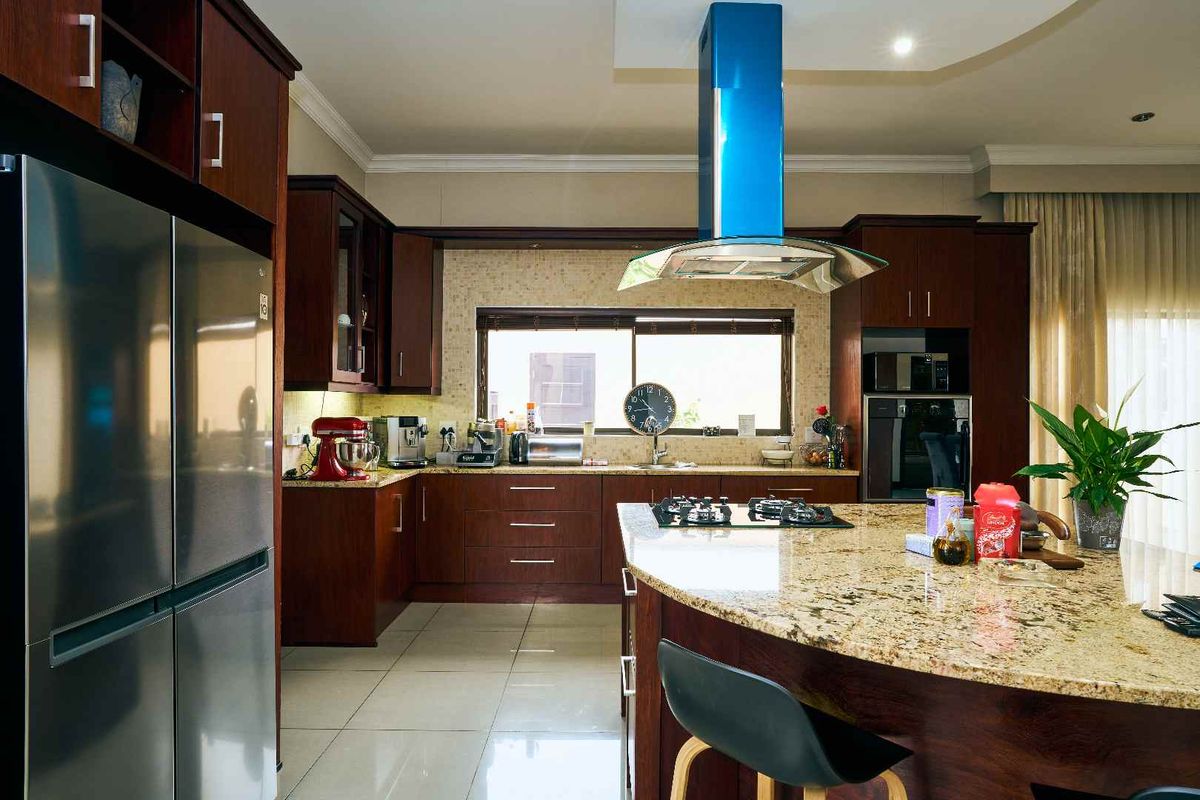 Spacious kitchen featuring dark wood cabinetry, granite countertops, a central island with a gas hob, and a modern stainless steel extractor fan.