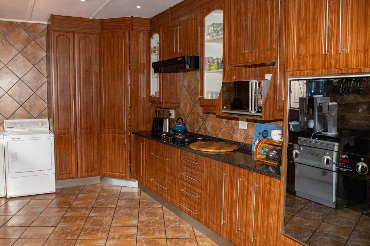A functional kitchen featuring wood-grain cabinetry, granite countertops, tiled flooring, and built-in appliances including an oven, hob, and extractor fan.