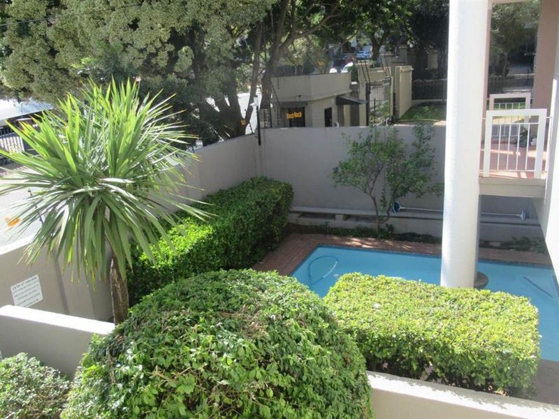 An elevated view of a private swimming pool area featuring landscaped hedges, a boundary wall, and an adjacent balcony structure.