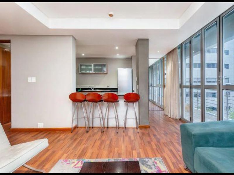 Modern open-plan living and kitchen area featuring hardwood flooring, recessed lighting, and expansive glass sliding doors leading to an outdoor space.