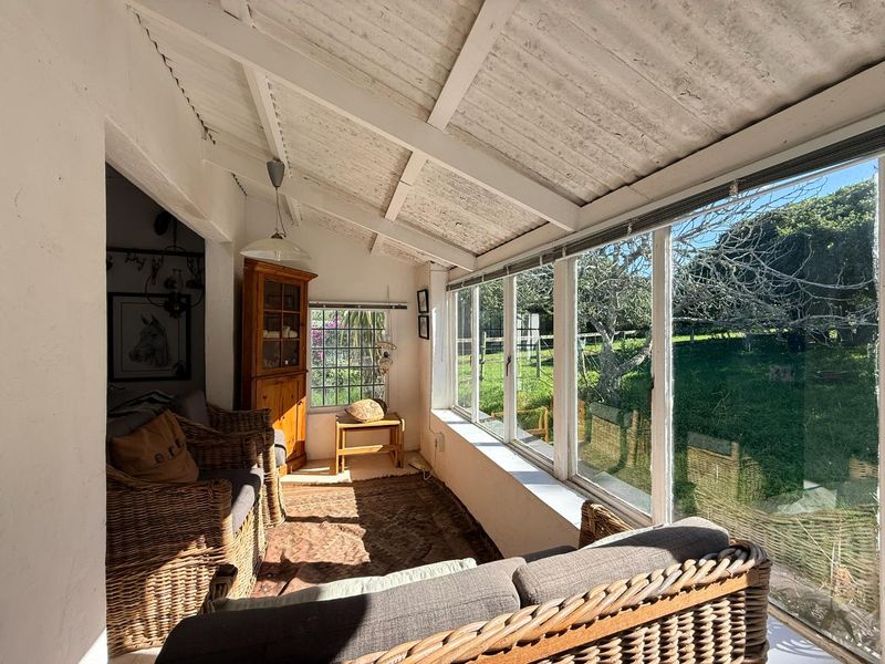 A sun-drenched enclosed patio featuring exposed timber rafters and expansive windows overlooking the garden, offering a bright and versatile living space.