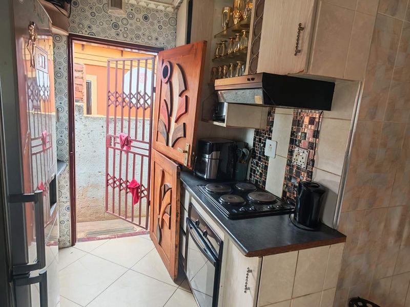 Compact kitchen featuring built-in oven, electric hob, extractor fan, and tiled splashback, with direct access to an exterior area via a security gate.