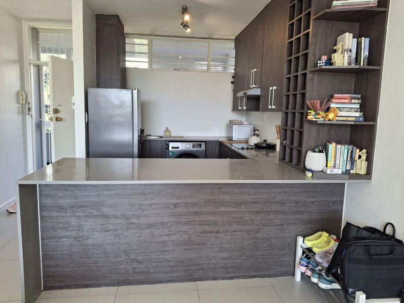 Modern kitchen featuring dark wood-grain cabinetry, stone countertops, a breakfast bar, and integrated shelving, providing a functional and stylish cooking space.