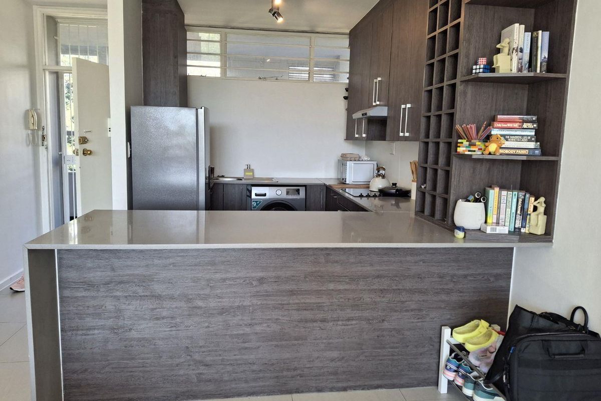 Modern kitchen featuring dark wood-grain cabinetry, stone countertops, a breakfast bar, and integrated shelving, providing a functional and stylish cooking space.