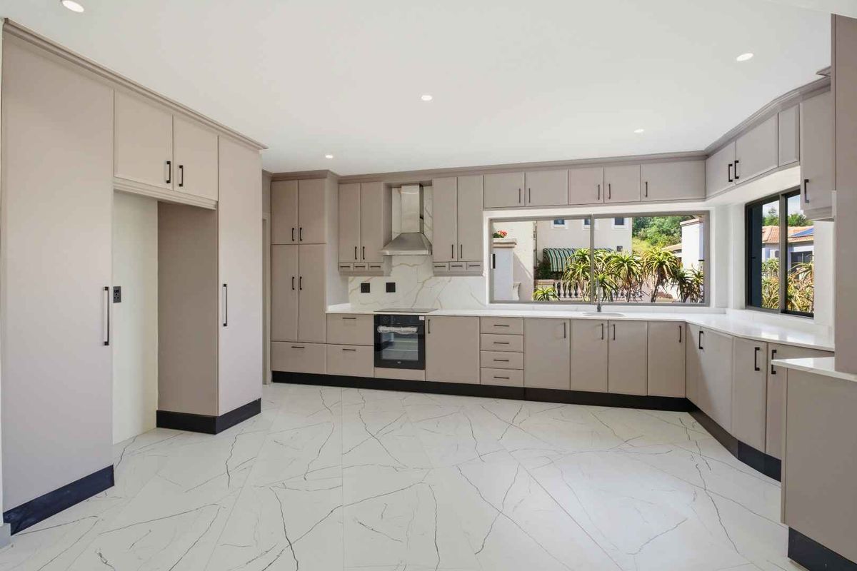 Modern kitchen featuring sleek cabinetry, integrated oven, stainless steel extractor fan, and marble-look tiled flooring with a bright, clean aesthetic.