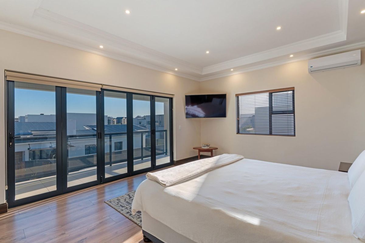 Spacious bedroom featuring wood-look flooring, recessed ceiling lighting, a wall-mounted air conditioning unit, and large sliding glass doors opening to a private balcony.