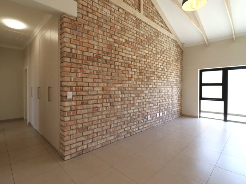 Spacious living area featuring a striking exposed brick wall, vaulted ceilings with timber rafters, tiled flooring, and ample built-in storage.