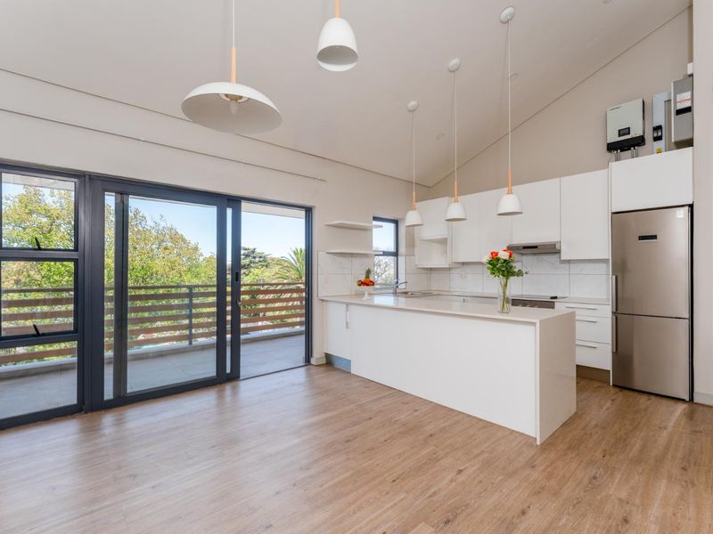 Modern open-plan kitchen and living area featuring sleek white cabinetry, stone countertops, laminate flooring, and large sliding doors leading to a private balcony.