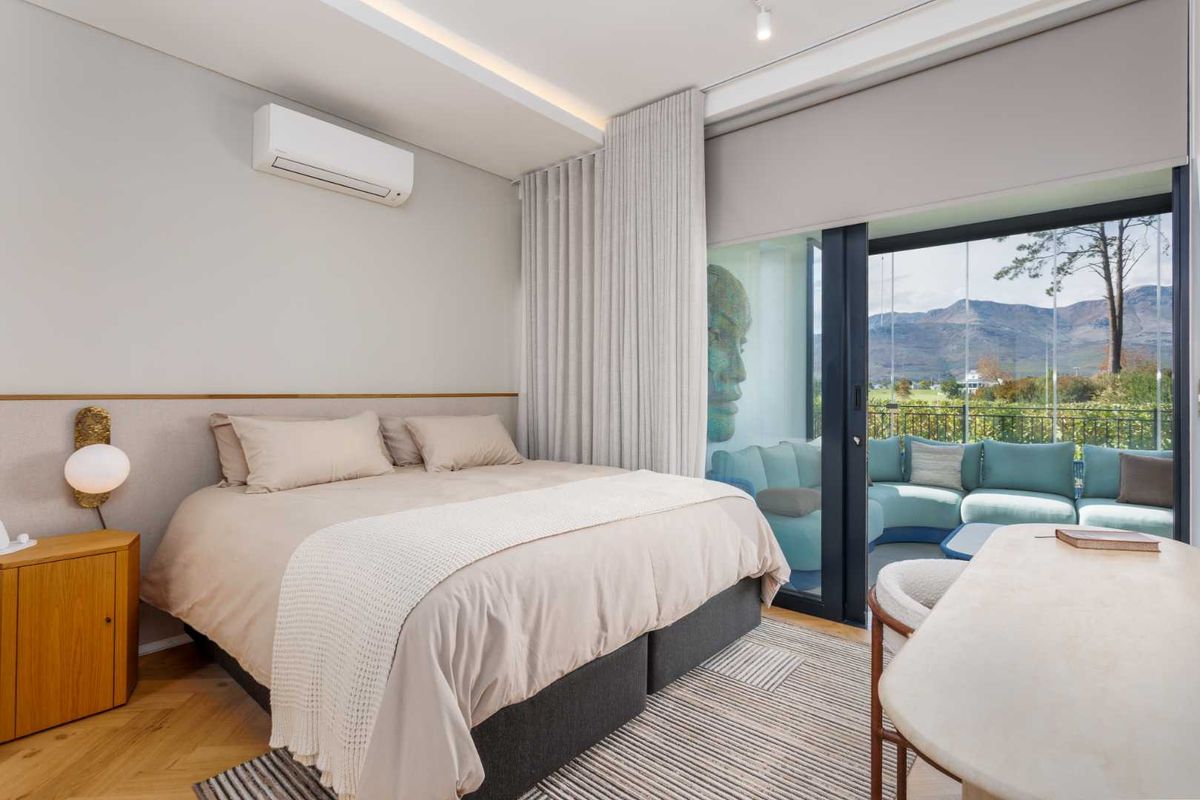 Modern bedroom featuring herringbone timber flooring, recessed ceiling lighting, wall-mounted air conditioning unit, and large sliding glass doors opening to a private balcony with views.