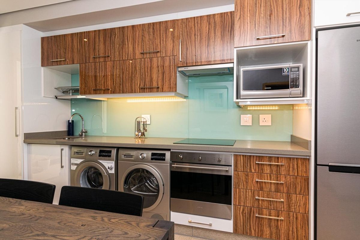 Modern kitchen featuring wood-grain cabinetry, stone countertops, glass splashback, and integrated appliances including an oven, hob, and microwave.