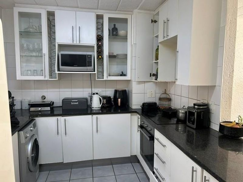 A functional kitchen featuring white cabinetry, dark granite countertops, a built-in oven, hob, and an integrated washing machine with tiled backsplash.