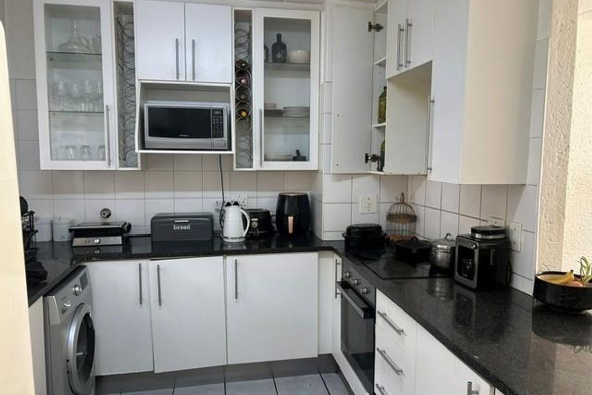 A functional kitchen featuring white cabinetry, dark granite countertops, a built-in oven, hob, and an integrated washing machine with tiled backsplash.