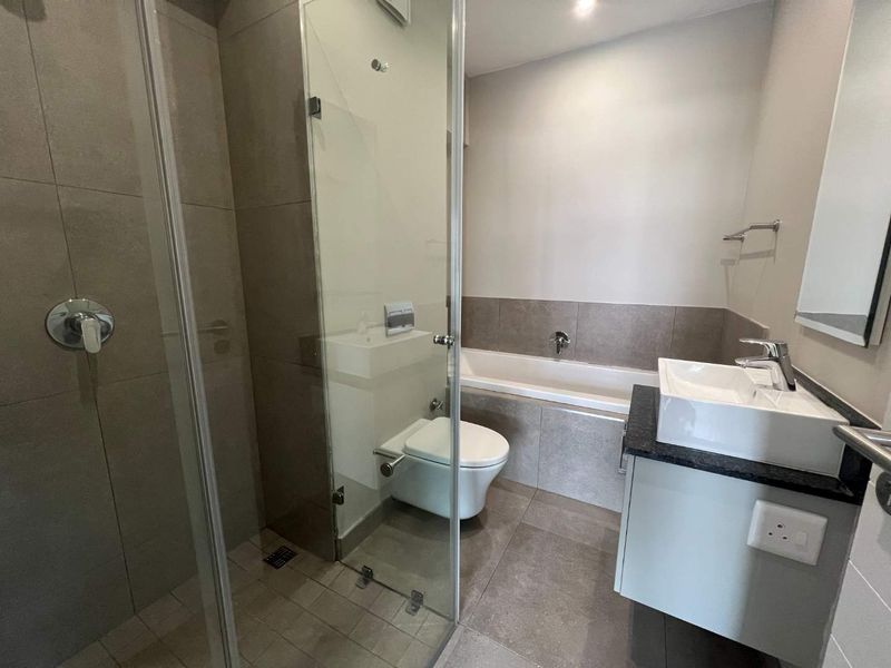 Modern bathroom featuring a glass-enclosed shower, built-in bathtub, wall-mounted toilet, and a sleek vanity with a countertop basin.