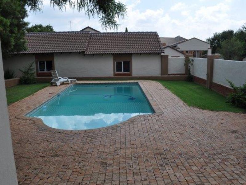 A private backyard featuring a swimming pool surrounded by brick paving and a boundary wall.