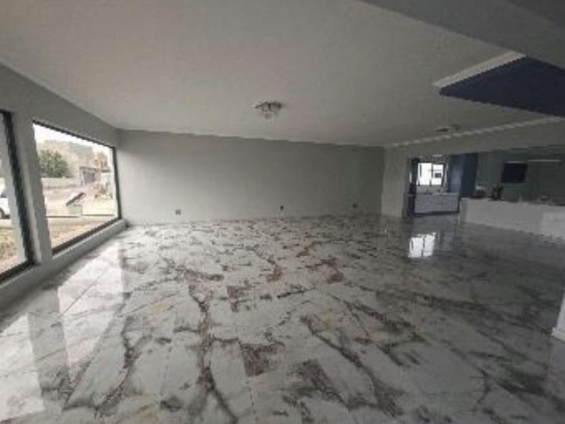 Spacious open-plan living area featuring polished marble-look floor tiles, large windows for natural light, and a seamless transition to the kitchen area.
