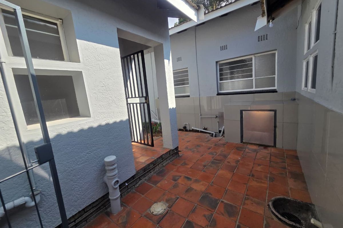A functional rear courtyard area featuring tiled flooring, a built-in braai, and direct access to the home via a security gate.
