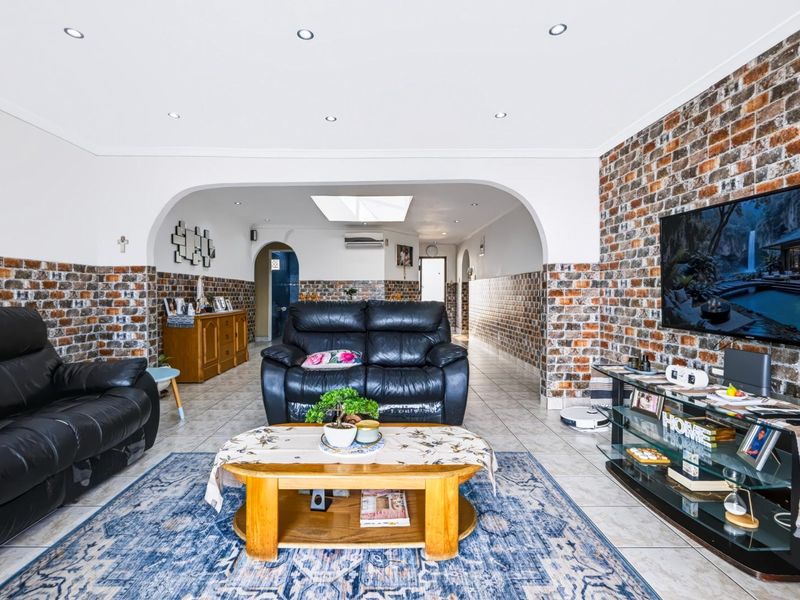 Spacious living area featuring exposed brick wall accents, recessed downlighting, a central archway, and a skylight, creating a bright and textured interior space.