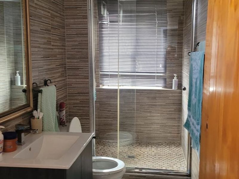 A functional bathroom featuring a modern vanity, a glass-enclosed shower, and neutral-toned wall tiling throughout.