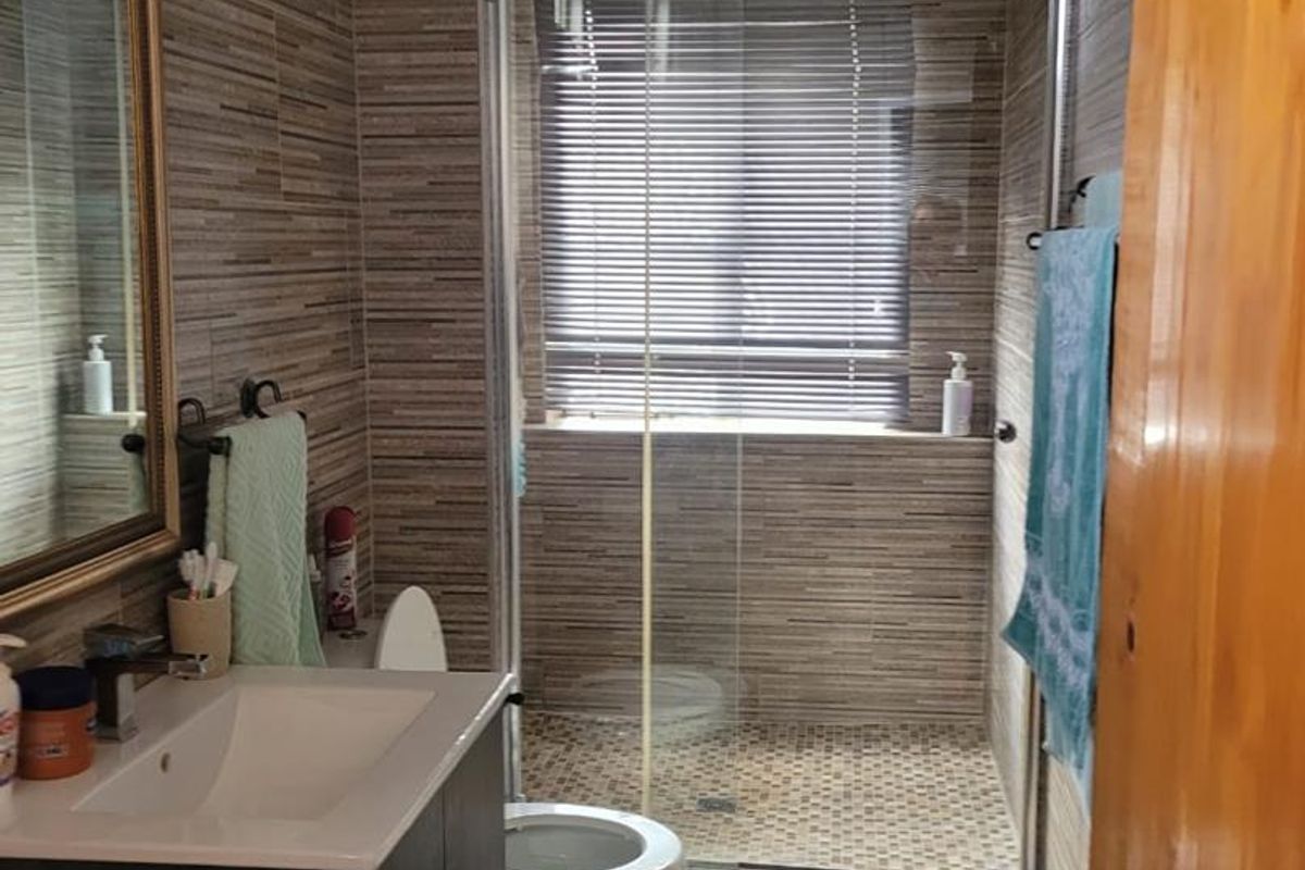 A functional bathroom featuring a modern vanity, a glass-enclosed shower, and neutral-toned wall tiling throughout.
