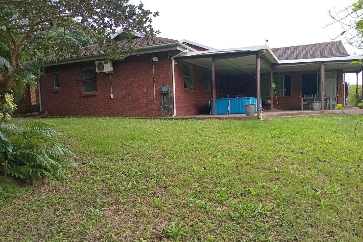 Rear view of a brick house featuring a covered patio area and a spacious garden.