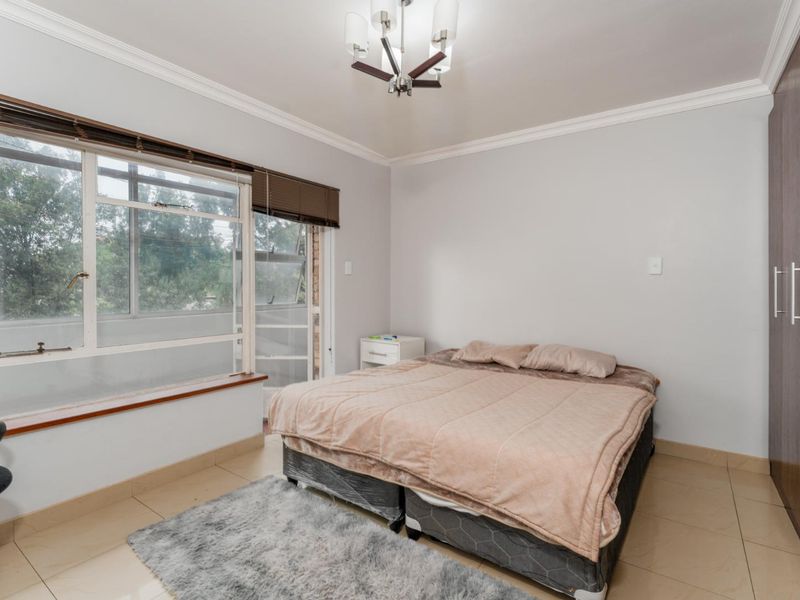 A well-lit bedroom featuring tiled flooring, a built-in wardrobe, and large windows that provide natural light and a view of the exterior.