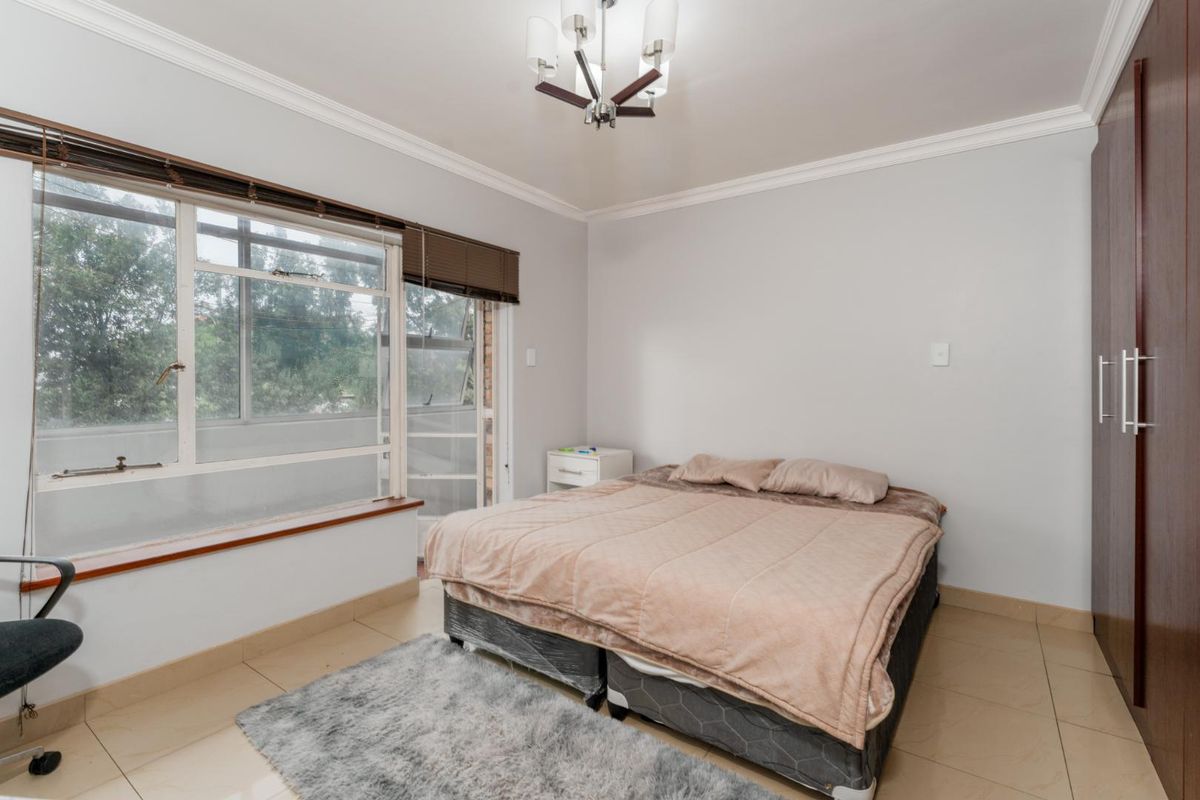 A well-lit bedroom featuring tiled flooring, a built-in wardrobe, and large windows that provide natural light and a view of the exterior.