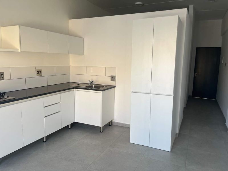 A clean, modern kitchen featuring white cabinetry, dark countertops, a built-in hob, and tiled flooring in an open-plan layout.