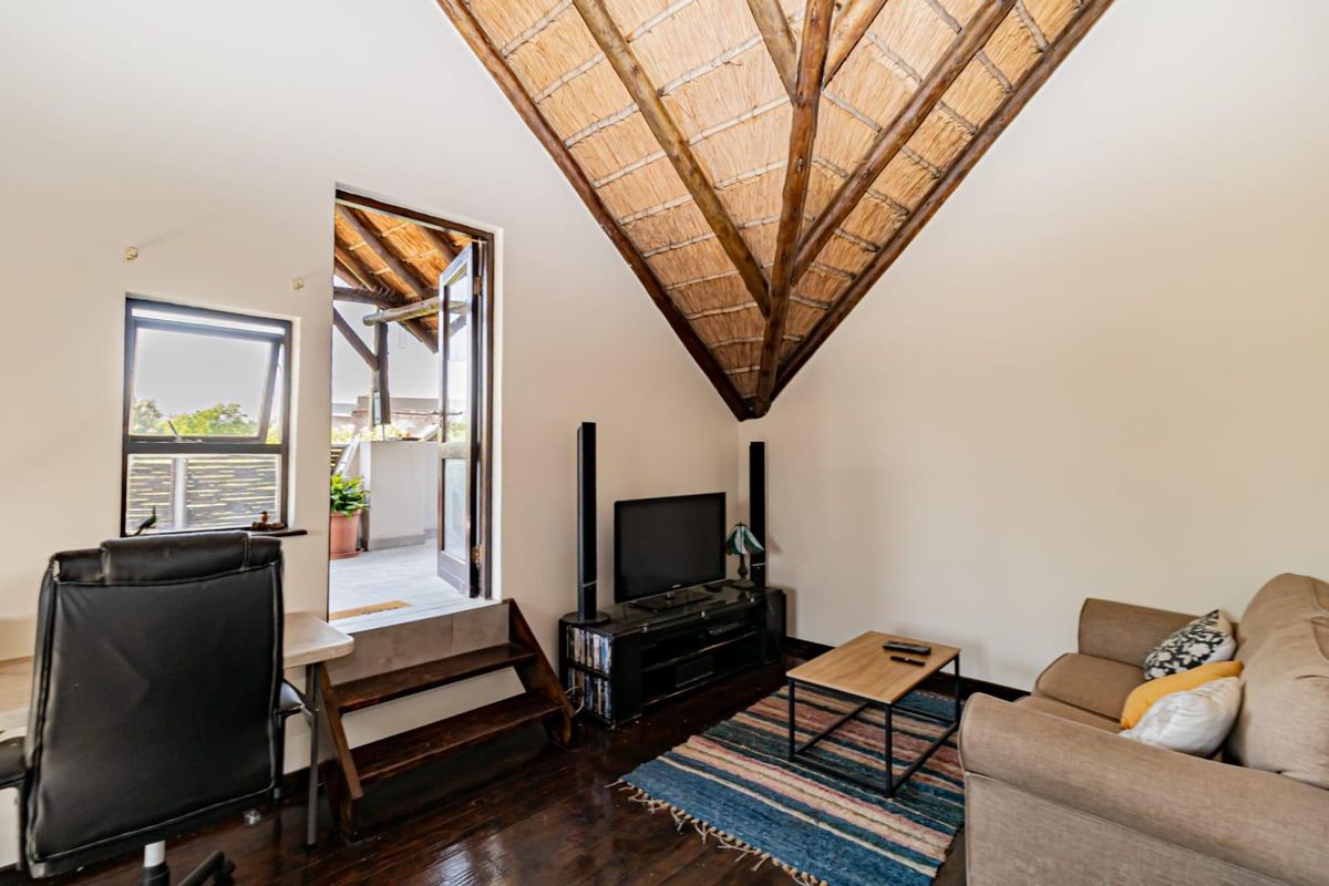 A cozy living room featuring a high vaulted thatched ceiling with exposed timber rafters, dark wood flooring, and direct access to an outdoor balcony.