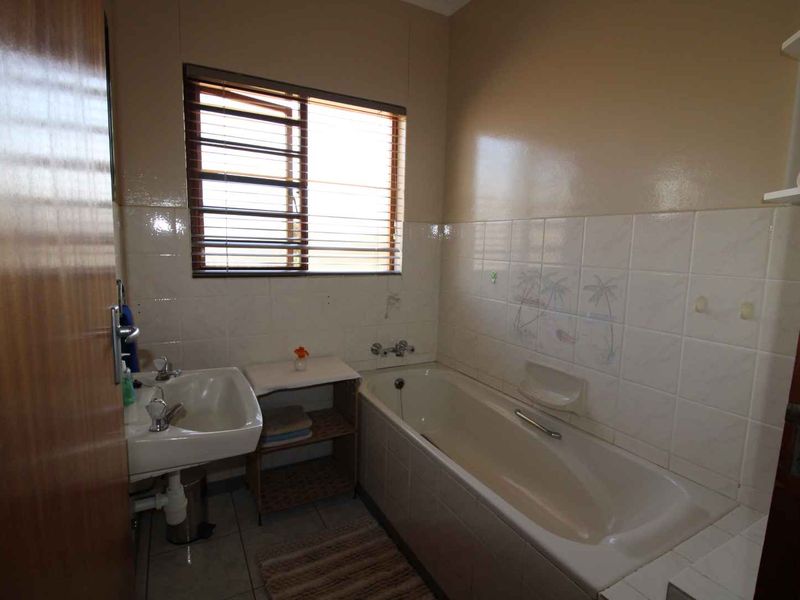 A dated bathroom featuring a standard bathtub, wall-mounted basin, and tiled finishes, offering potential for modernization and cosmetic updates.