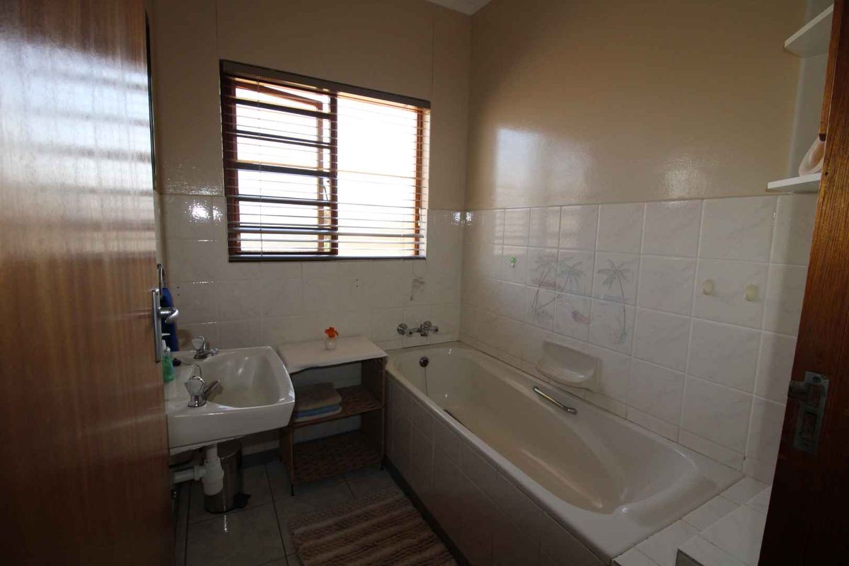 A dated bathroom featuring a standard bathtub, wall-mounted basin, and tiled finishes, offering potential for modernization and cosmetic updates.