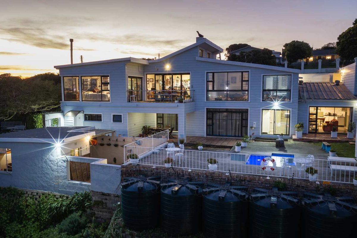 Rear view of a multi-level house featuring a swimming pool, timber deck, balcony, and multiple water storage tanks at dusk.
