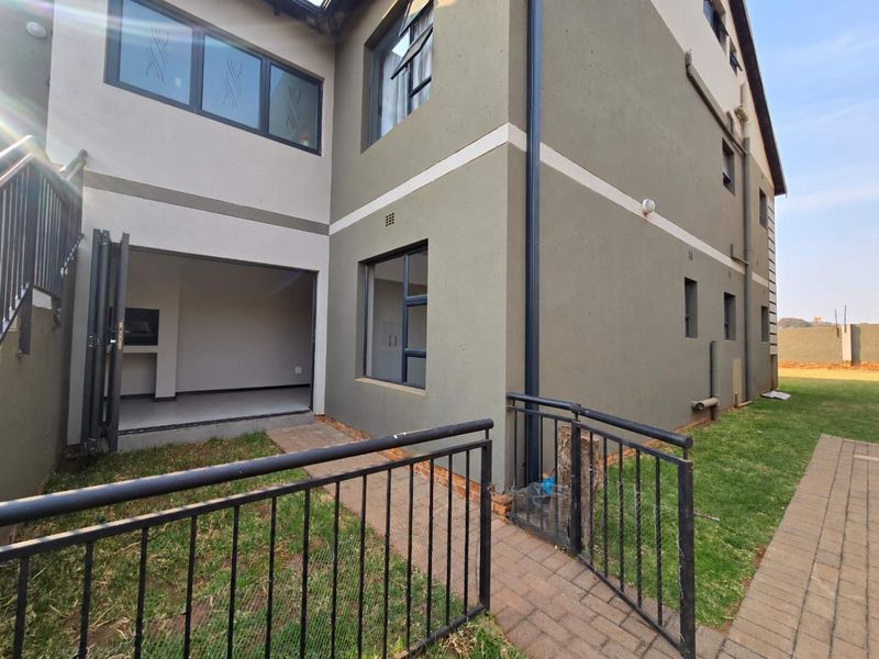 Rear exterior view of the apartment featuring a paved walkway, metal railings, and a covered patio area with a built-in braai.