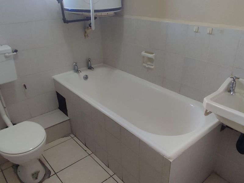 A dated bathroom featuring a standard bathtub, toilet, and wall-mounted basin with exposed plumbing and ceramic tiling throughout.
