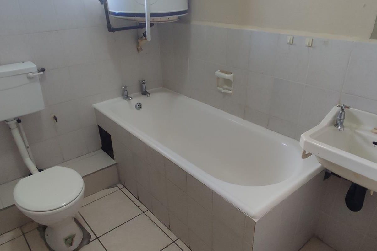 A dated bathroom featuring a standard bathtub, toilet, and wall-mounted basin with exposed plumbing and ceramic tiling throughout.