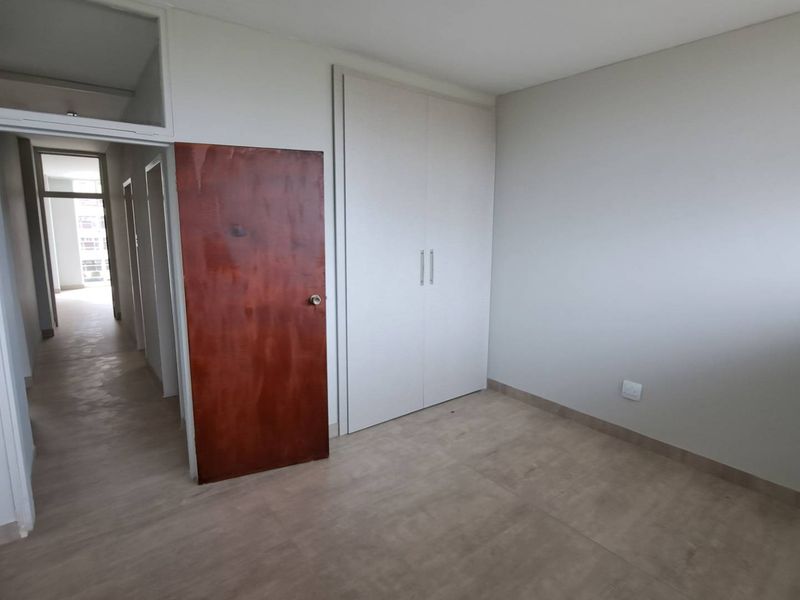 A clean, empty bedroom featuring neutral tiled flooring, a built-in wardrobe, and a wooden door leading to a hallway.