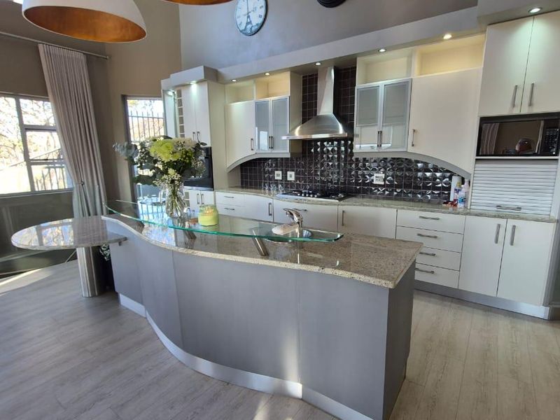 Modern kitchen featuring a curved granite island with a glass breakfast bar, ample built-in cabinetry, and high-quality integrated appliances.