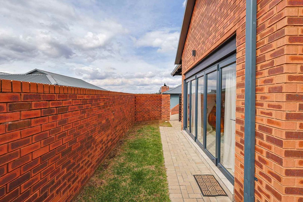 A side view of the townhouse featuring a brick boundary wall, a paved walkway, and modern bi-fold glass doors leading into the interior.