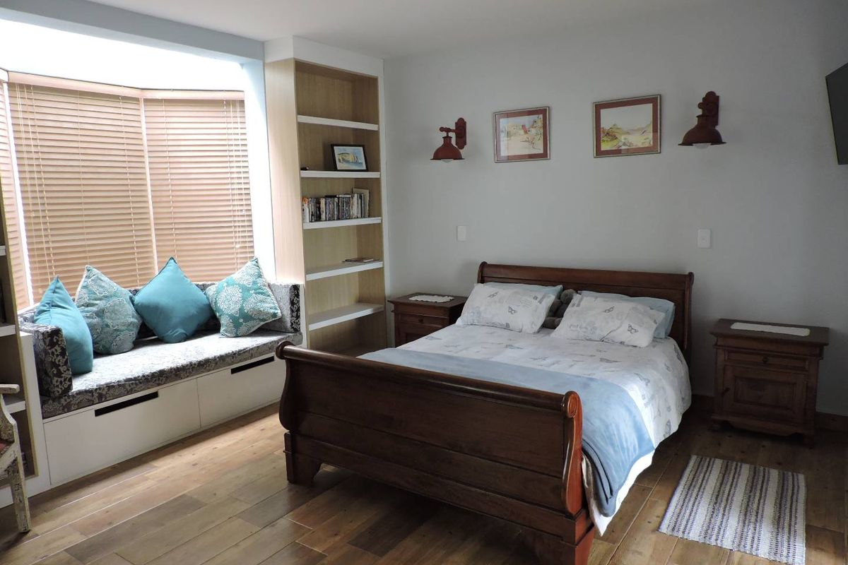 A well-maintained bedroom featuring built-in shelving, a custom window seat with storage, and warm timber flooring.