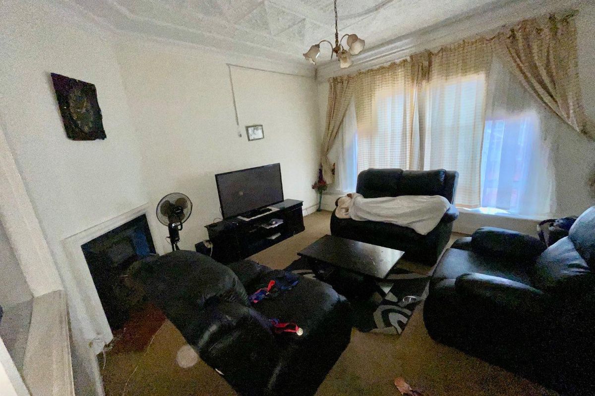 A living room featuring a traditional fireplace, decorative ceiling molding, and large windows, offering a classic layout with potential for modernization.
