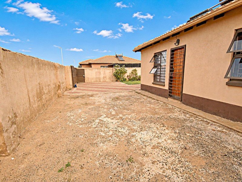 Rear exterior area featuring a paved driveway, perimeter walling, and security-fitted windows and doors, offering potential for landscaping and outdoor improvement.