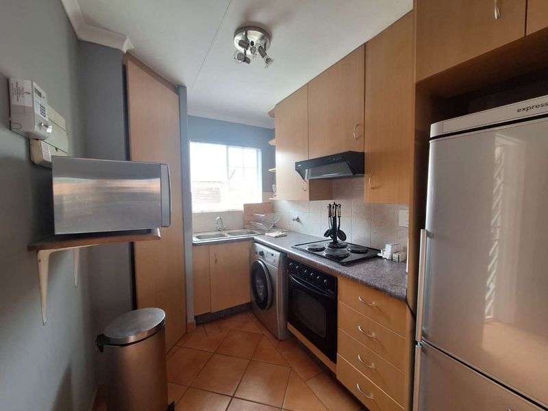 Compact kitchen featuring light wood cabinetry, laminate countertops, built-in oven with hob, extractor fan, and tiled flooring with a functional layout.