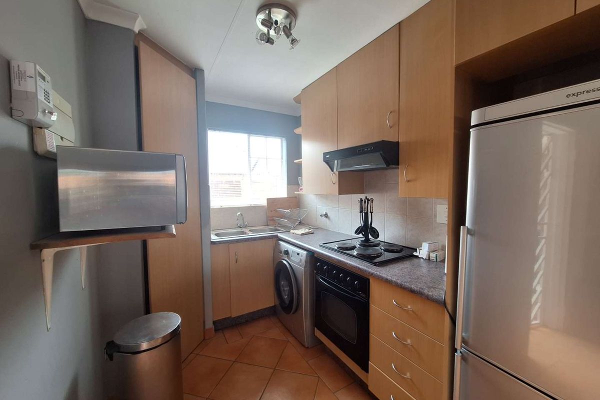 Compact kitchen featuring light wood cabinetry, laminate countertops, built-in oven with hob, extractor fan, and tiled flooring with a functional layout.