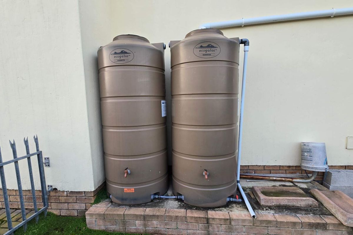 Two large brown rainwater storage tanks installed on a brick plinth against the exterior wall of the property.